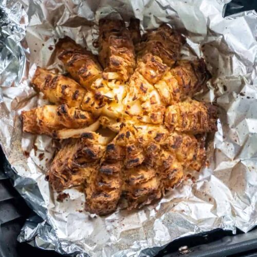 Closeup view of a prepared blooming onion on aluminum foil in a black air fryer basket.