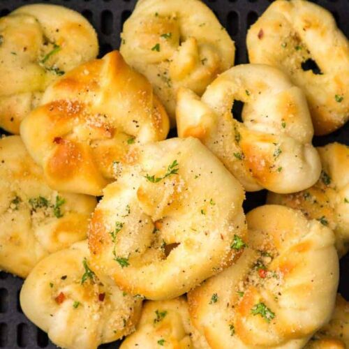 Close up view of prepared garlic knots with seasoning resting in a black air fryer basket.