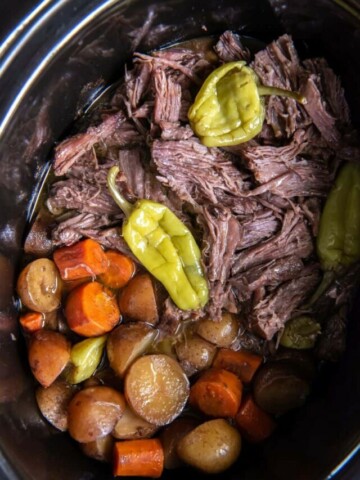 Close up view of prepared Mississippi Pot Roast and vegetables in a black slow cooker.