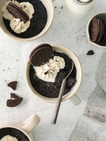 A spoon inside an oreo cake in a mug topped with whipped cream and whole oreos.