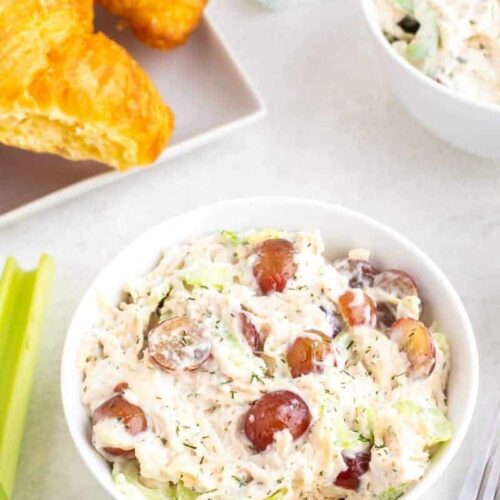 A bowl of chicken salad with a plate of croissants in the background.