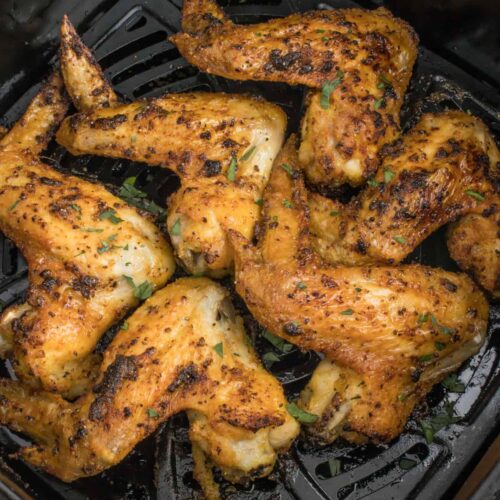 Seasoned chicken wings in a black air fryer basket after cooking.