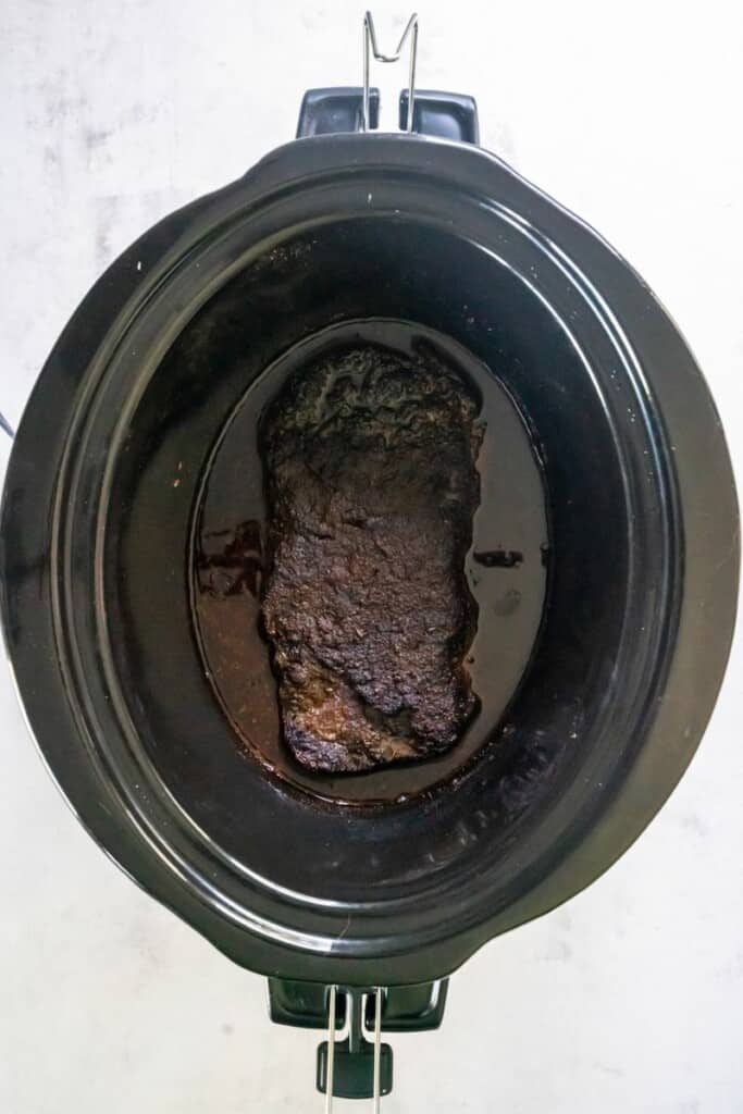 Seasoned skirt steak after cooking in a black crock pot.