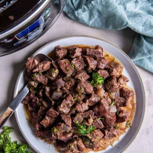 A serving of crock pot steak cubes on a plate next to a blue napkin.