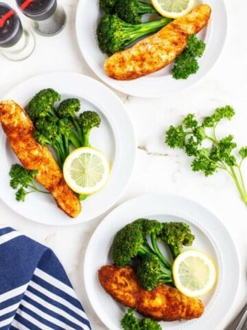 Overhead view of three plates of seasoned halibut with rice and broccoli.