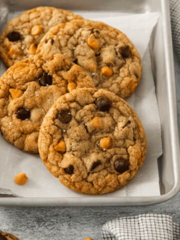 Four butterscotch chocolate chip cookies on a parchment lined baking sheet.