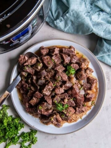 A serving of crock pot steak cubes on a plate next to a blue napkin.