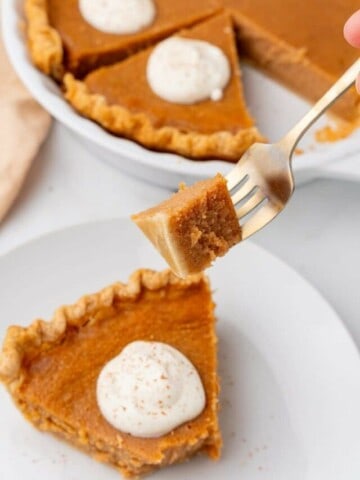 A fork holding a bite of sweet potato pie over a full slice on a plate.