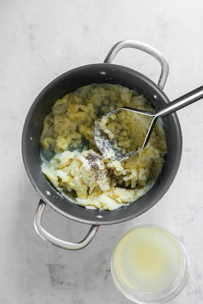 Using potato masher to mash potatoes in saucepan available as