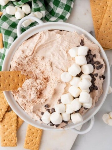 A bowl of hot cocoa dip topped with mini marshmallows and chocolate chips.