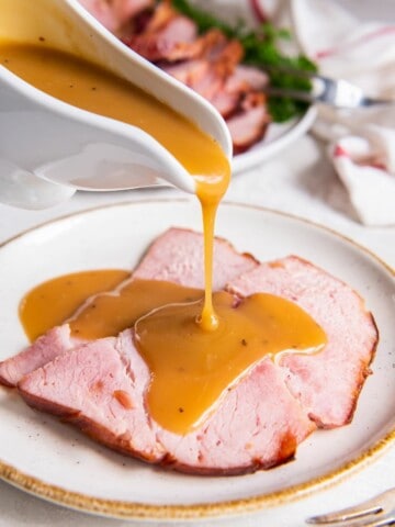 pouring ham gravy over slices of ham on a plate.