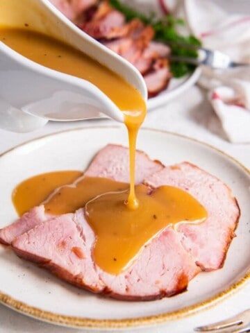 pouring ham gravy over slices of ham on a plate.