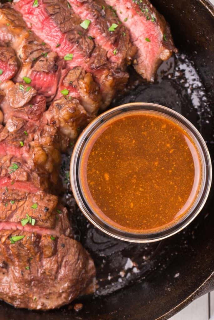 close up of cooked steak in a cast iron pan with the easy steak marinade in a mason jar.