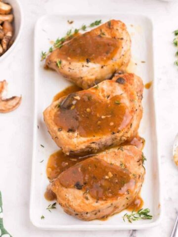 pork loin chops on a white plater with drizzled gravy and fresh thyme