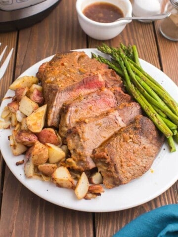 sliced tri tip on a white plate with roasted potatoes and asparagus