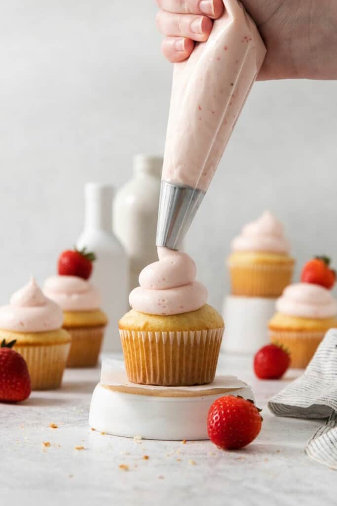 Piping frosting onto vanilla cupcakes.