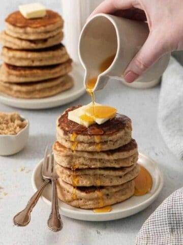 Pouring syrup onto stack of homemade pancakes.