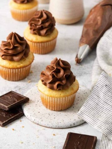 Piping bag filled with homemade cream cheese icing laid behind vanilla cupcakes.