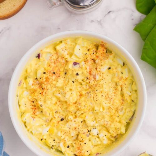 overhead shot of egg salad in a bowl seasoned with black pepper and paprika.