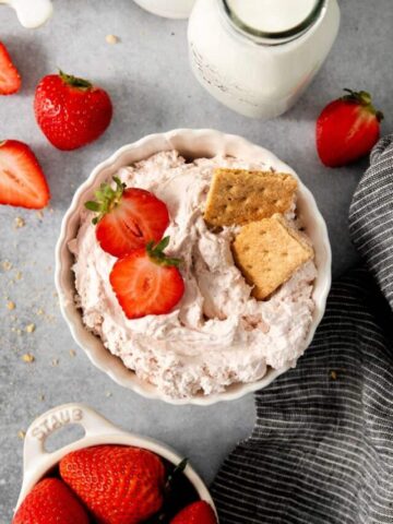 bowl of cream cheese based dip with sliced berries and graham crackers on top