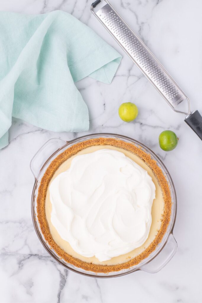 adding whipped topping on top of baked key lime pie