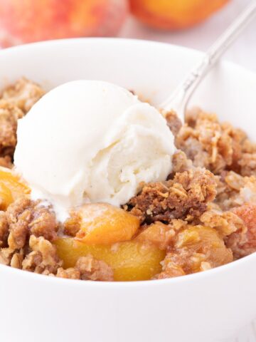 a bowl of peach crisp with oats and vanilla ice cream
