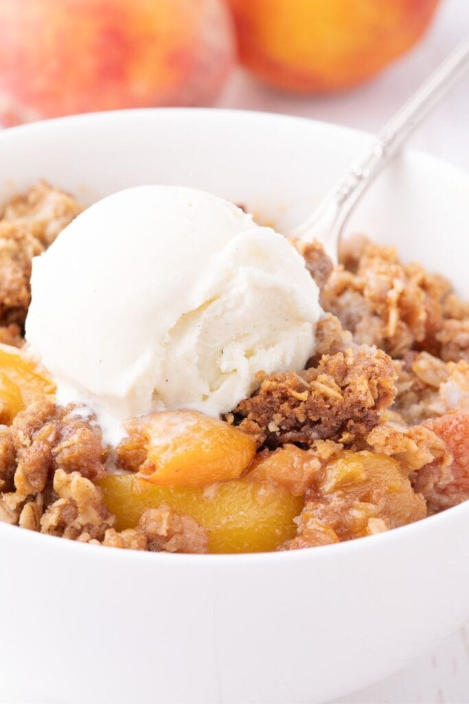 a bowl of peach crisp with oats and vanilla ice cream