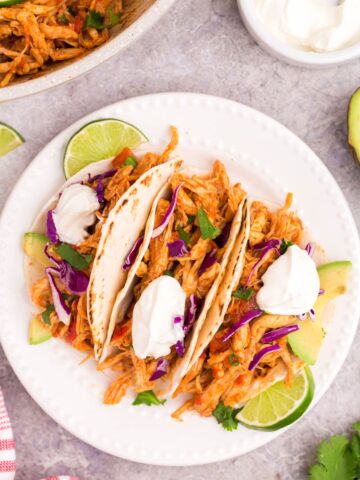 overhead picture of pulled chicken tacos on a white plate with limes