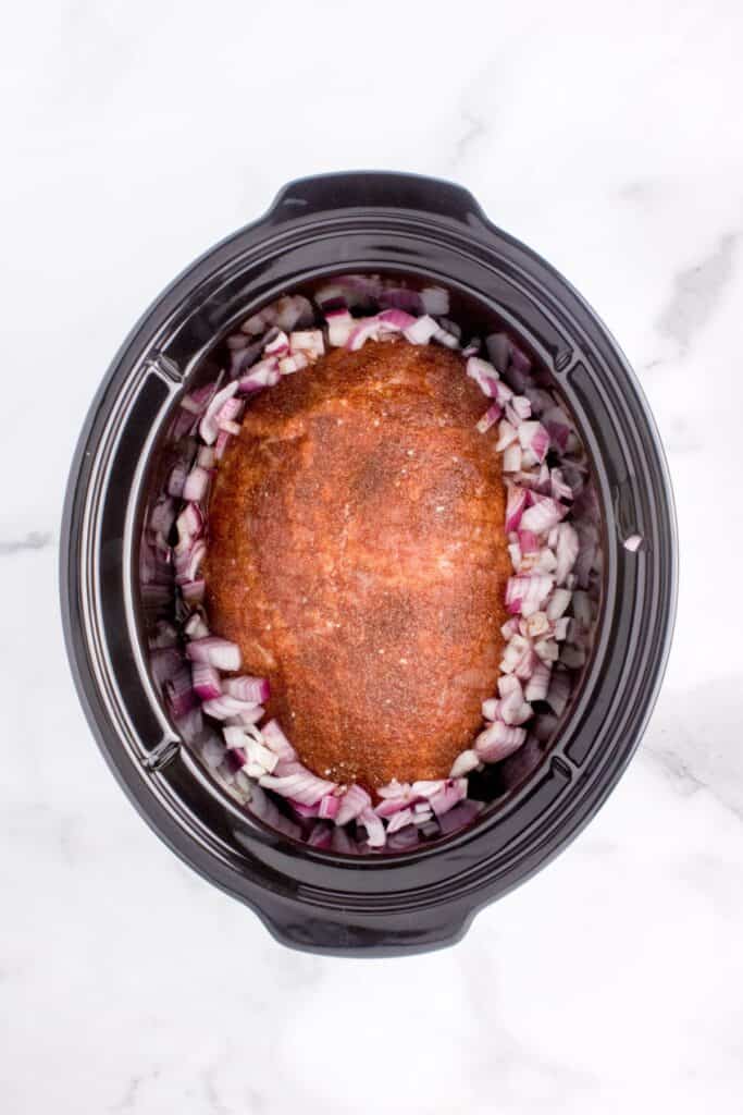 adding seasoned pork butt to slow cooker with red onions