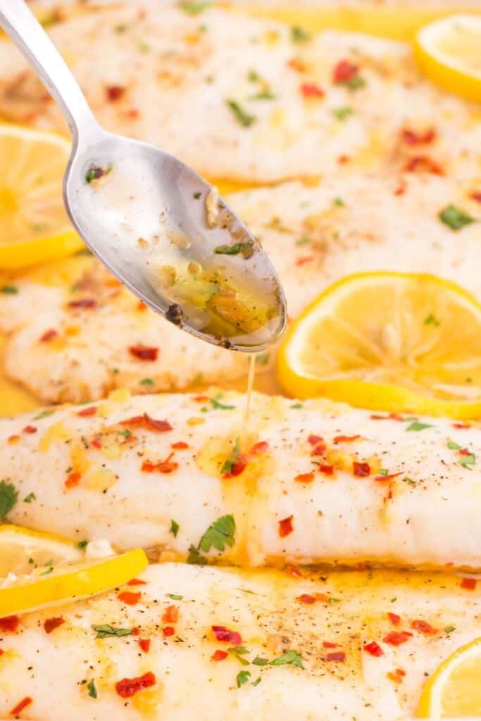 drizzling garlic butter over tender tilapia fish 