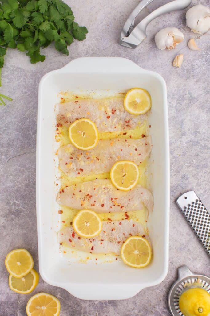 adding raw tilapia filets to a baking dish with butter and lemon