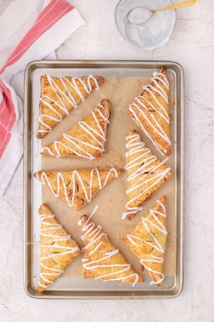 Parchment paper lined baking sheet with 8 baked and iced apple turnovers.