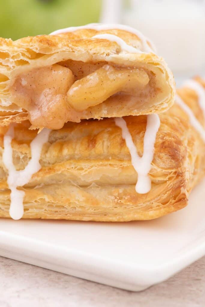 Stacked apple turnovers on a white plate. The top apple turnover is sliced open to show the baked filling inside.