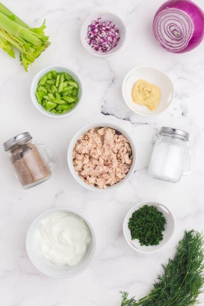 Flatlay of Tuna Salad ingredients. Canned tuna, mayonnaise, chopped celery, chopped red onion, dijon mustard, fresh dill, salt and pepper.