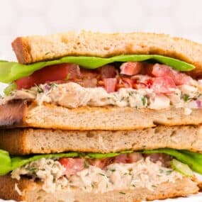 Two halves of a tuna sandwich stacked on one another on a white plate.