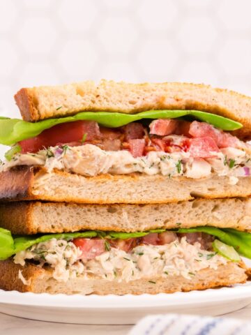 Two halves of a tuna sandwich stacked on one another on a white plate.