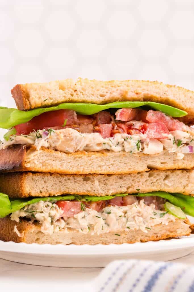 Two halves of a tuna sandwich stacked on one another on a white plate.