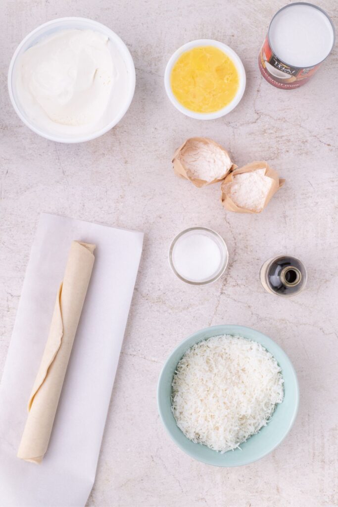 Coconut Cream Pie flatlay of ingredients. Coconut milk, whisked egg in a small bowl, 2 packages of vanilla pudding, vanilla extract, salt, sweetened shredded coconut, and Cool Whip.