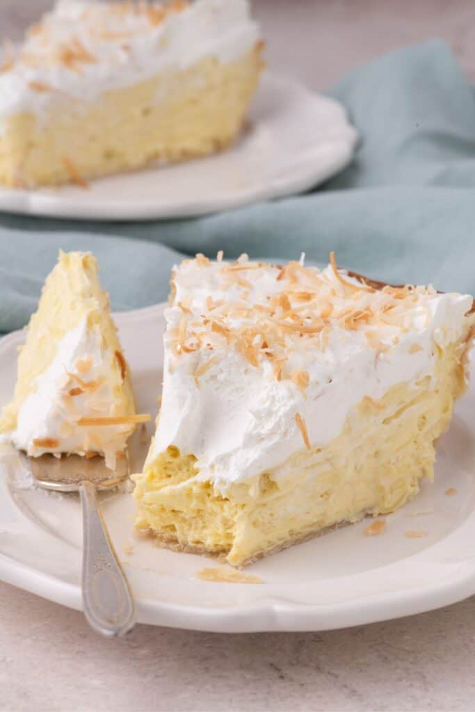 Forkful of coconut cream pie on a white plate with a cross section view of the layers of the pie.