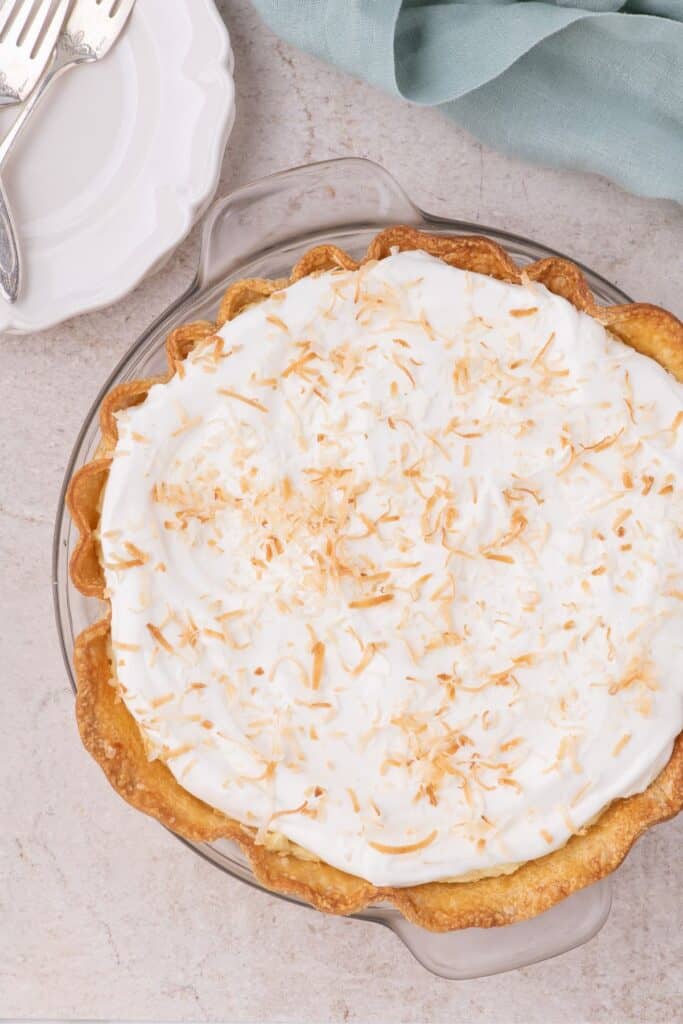 Completed Coconut Cream Pie, two serving plates with forks on the top left corner, a blue napkin on the top right corner.