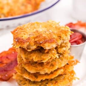 Stack of hash browns on a plate with bacon and a condiment bowl of ketchup.