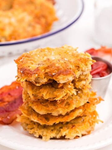 Stack of hash browns on a plate with bacon and a condiment bowl of ketchup.