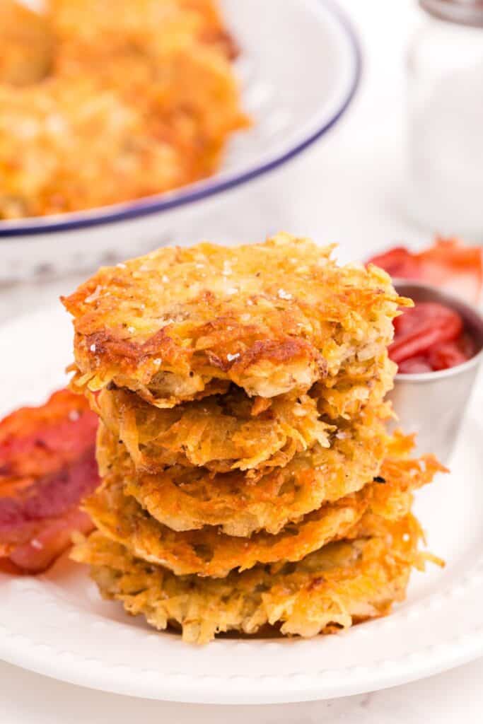 Stack of hash browns on a plate with bacon and a condiment bowl of ketchup.