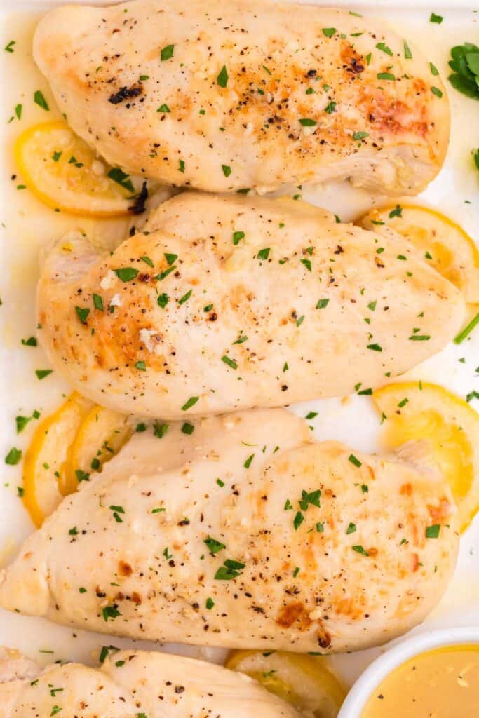 Close up of cooked lemon chicken on a serving tray with lemon and parsley garnishes