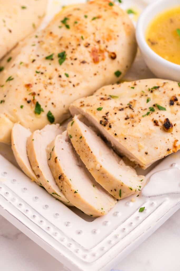 Sliced lemon chicken on a platter with lemon butter on the side.