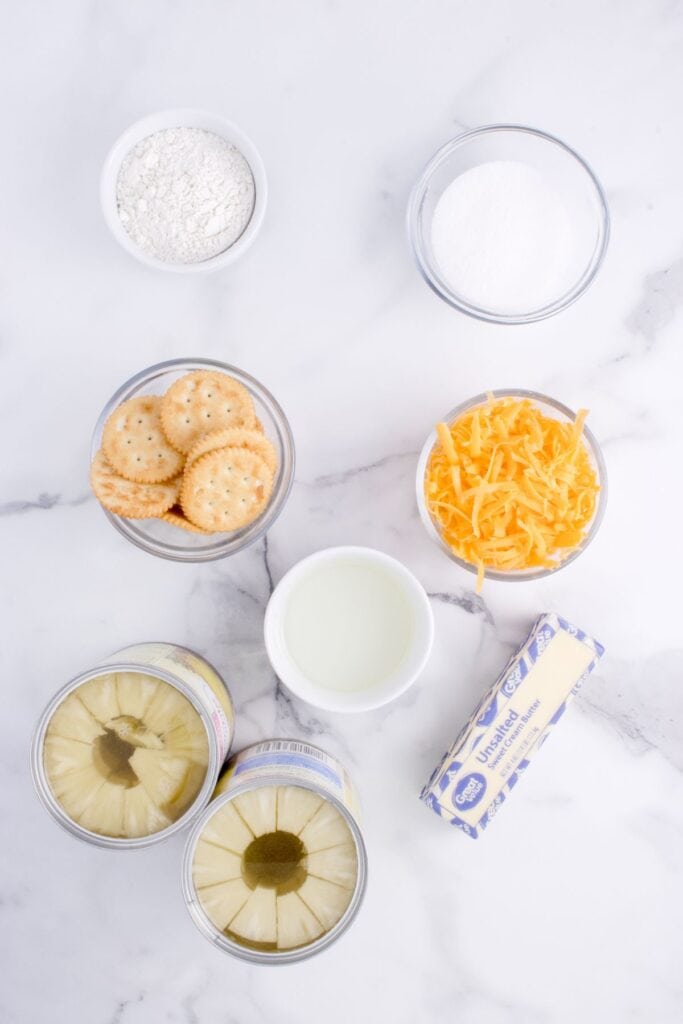Ingredient flatlay for Pineapple Casserole. Canned pineapple, butter, sugar, cheddar cheese, Ritz crackers, and flour.