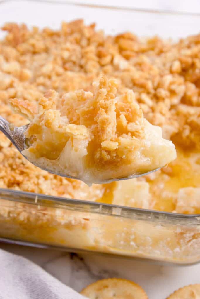 Spoonful of pineapple casserole in front of a baking dish of pineapple casserole.