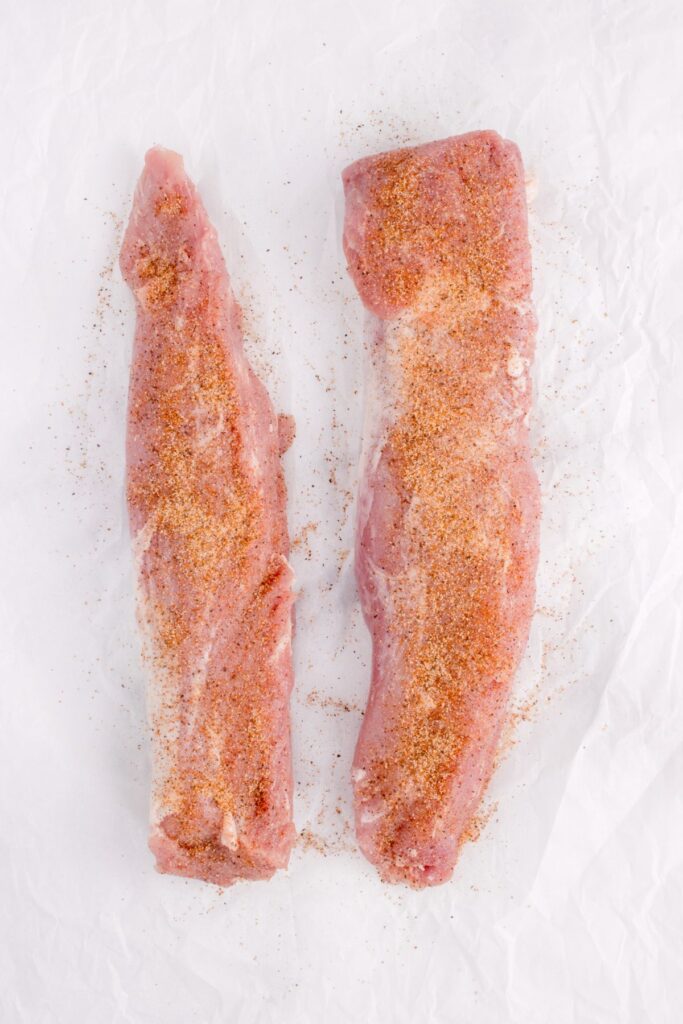 Two pork tenderloins unwrapped on butcher paper, coated with cajun seasoning.