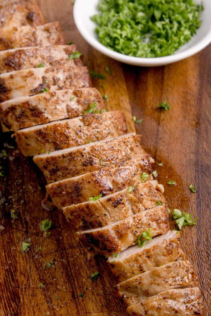 Cooked and sliced pork tenderloin, garnished with parsley.