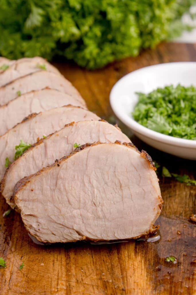 Close up view of cooked and sliced pork tenderloin with fresh parsley in the background.